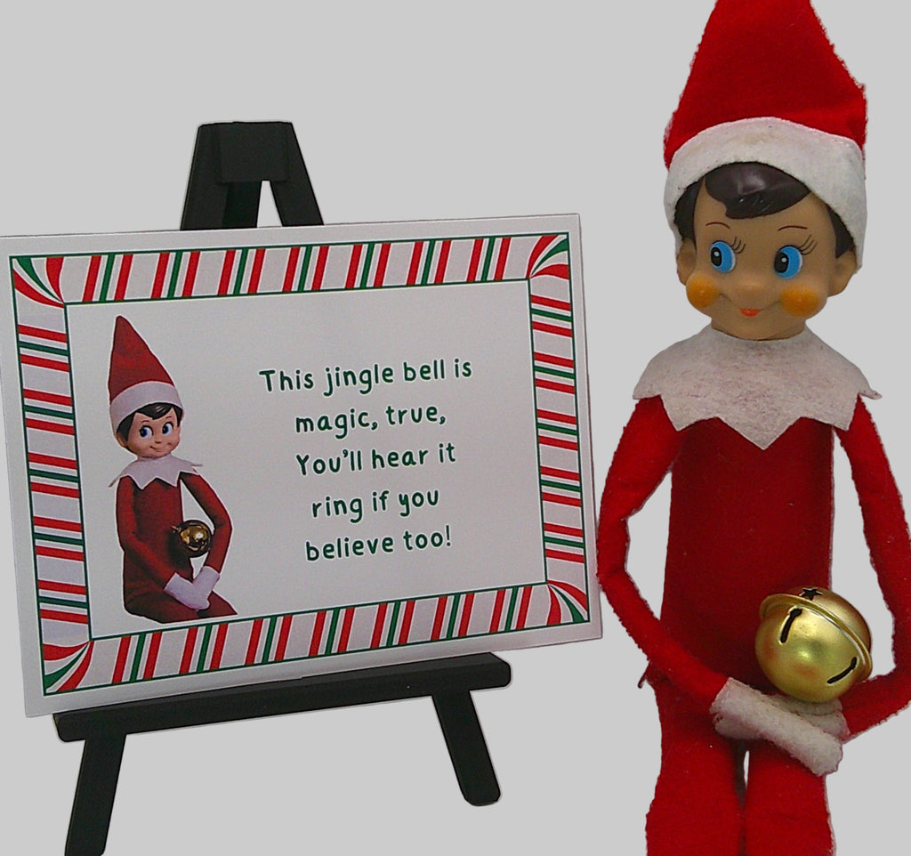 Elf on the Shelf with a sign and jingle bell, against a plain background