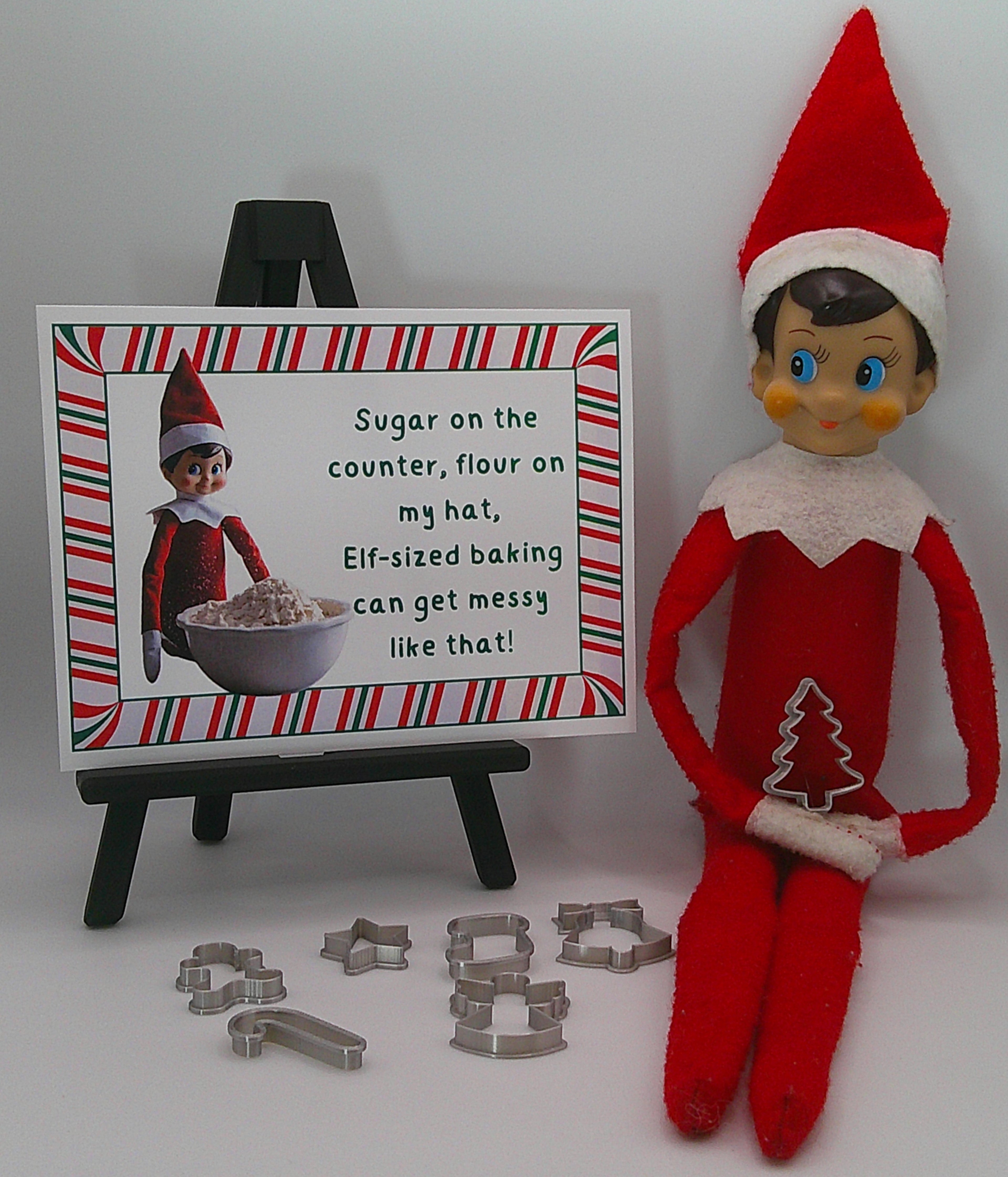 Elf on the Shelf with a sign and cookie cutters on a white background
