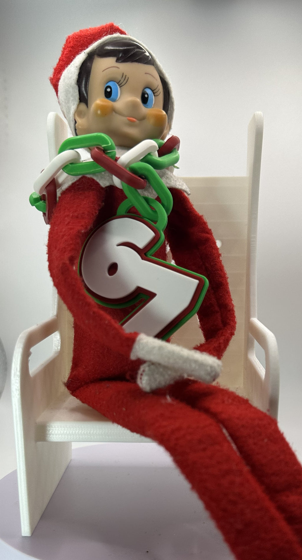 Elf on the Shelf figurine sitting on a chair with a white background